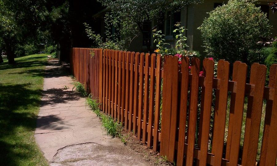 Stained picket fence along a sidewalk